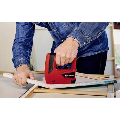A person in a denim shirt is attaching a canvas to a wooden frame using a red staple gun.