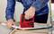 A person in a denim shirt is attaching a canvas to a wooden frame using a red staple gun.