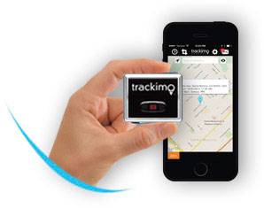 A hand holds a GPS tracking device in front of a smartphone displaying a map with a tracked route.