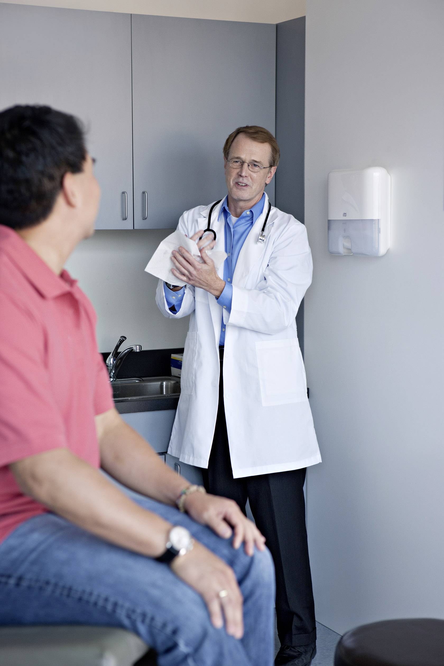 A doctor is speaking with a patient on a medical examination couch in a consulting room.