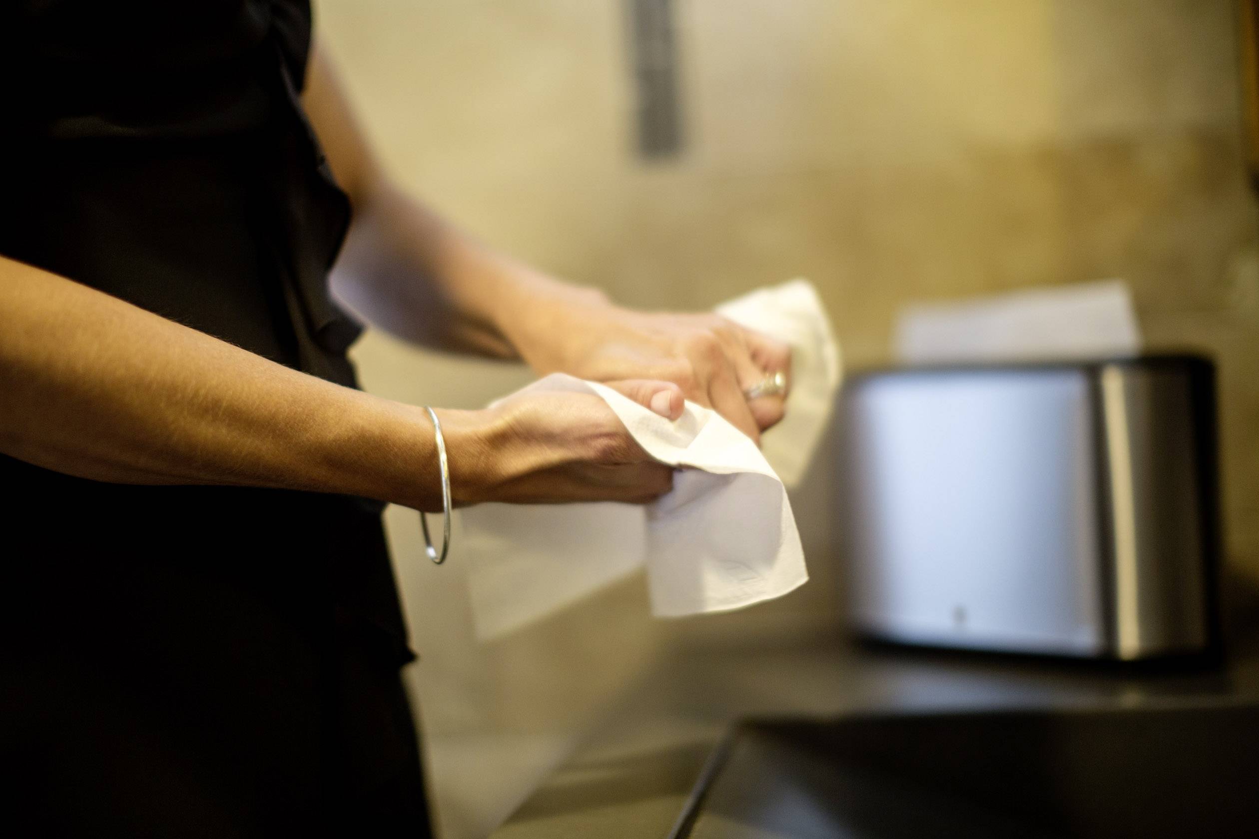 A person is drying their hands with a white paper towel in a kitchen. A shiny toaster stands in the background.