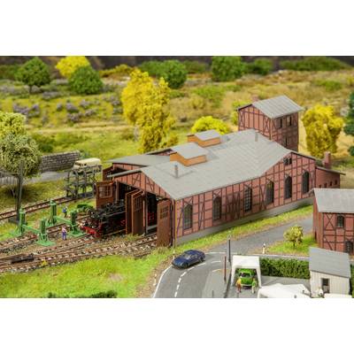 Miniature steam locomotive in a model railway depot with sliding doors. Landscape in the background with trees and roads.