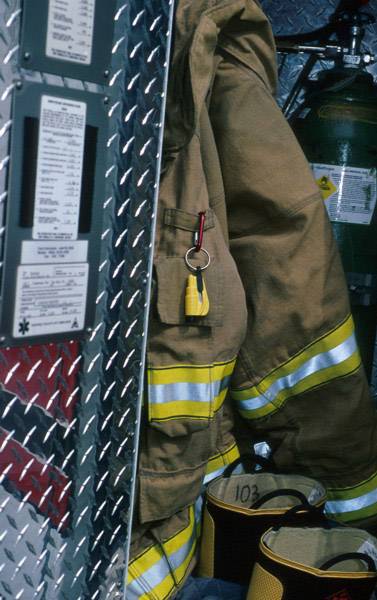 Firefighter's uniform hangs on the wall next to equipment items. Beside it is a container with hazard symbols.