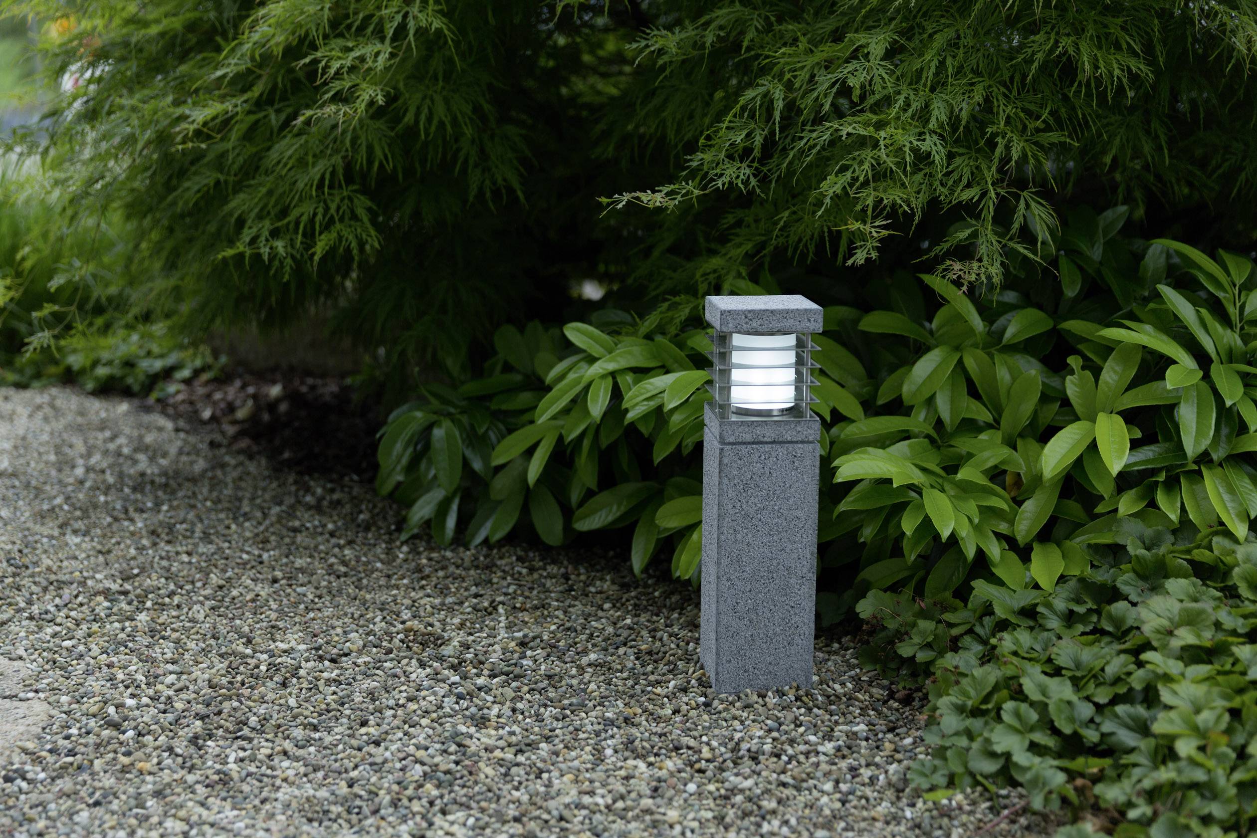 Outdoor light on a gravel path, surrounded by green plants, provides illumination in a garden area.