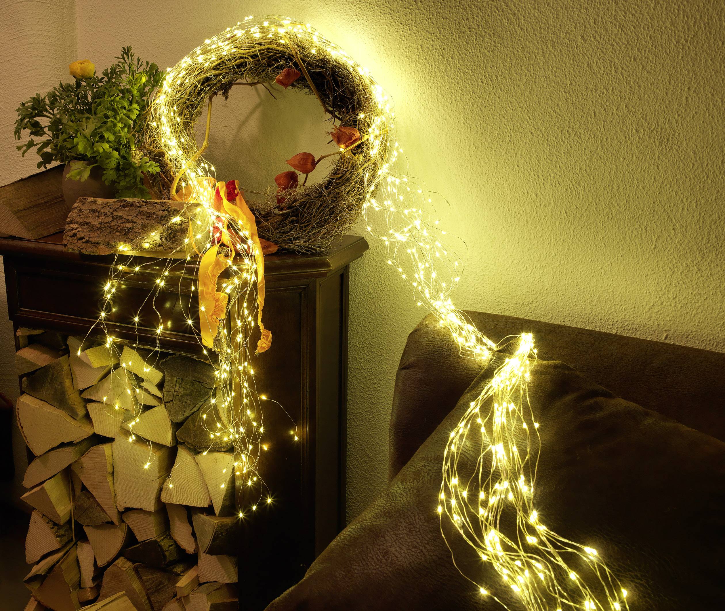 Wreath decorated with yellow LED lights, placed on the mantelpiece, with wooden logs in the background. Festive atmosphere with warm lighting.