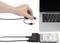 A hand is holding a USB cable over a laptop, with an external hard drive nearby, connected via an adapter to a second USB cable.