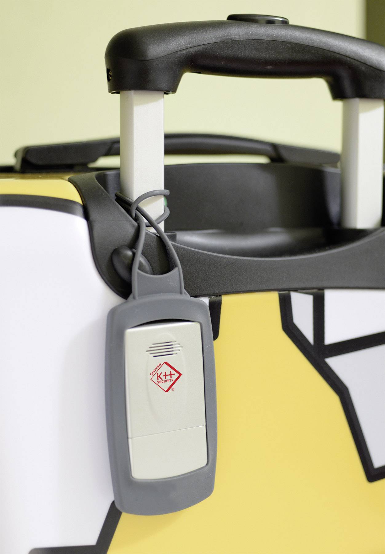 Yellow suitcase with a black and white pattern and a small grey lock on the handle. In the foreground, a security tag with a red symbol.