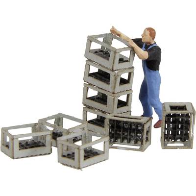 A man in workwear is stacking metal crates. Some crates are lying nearby.