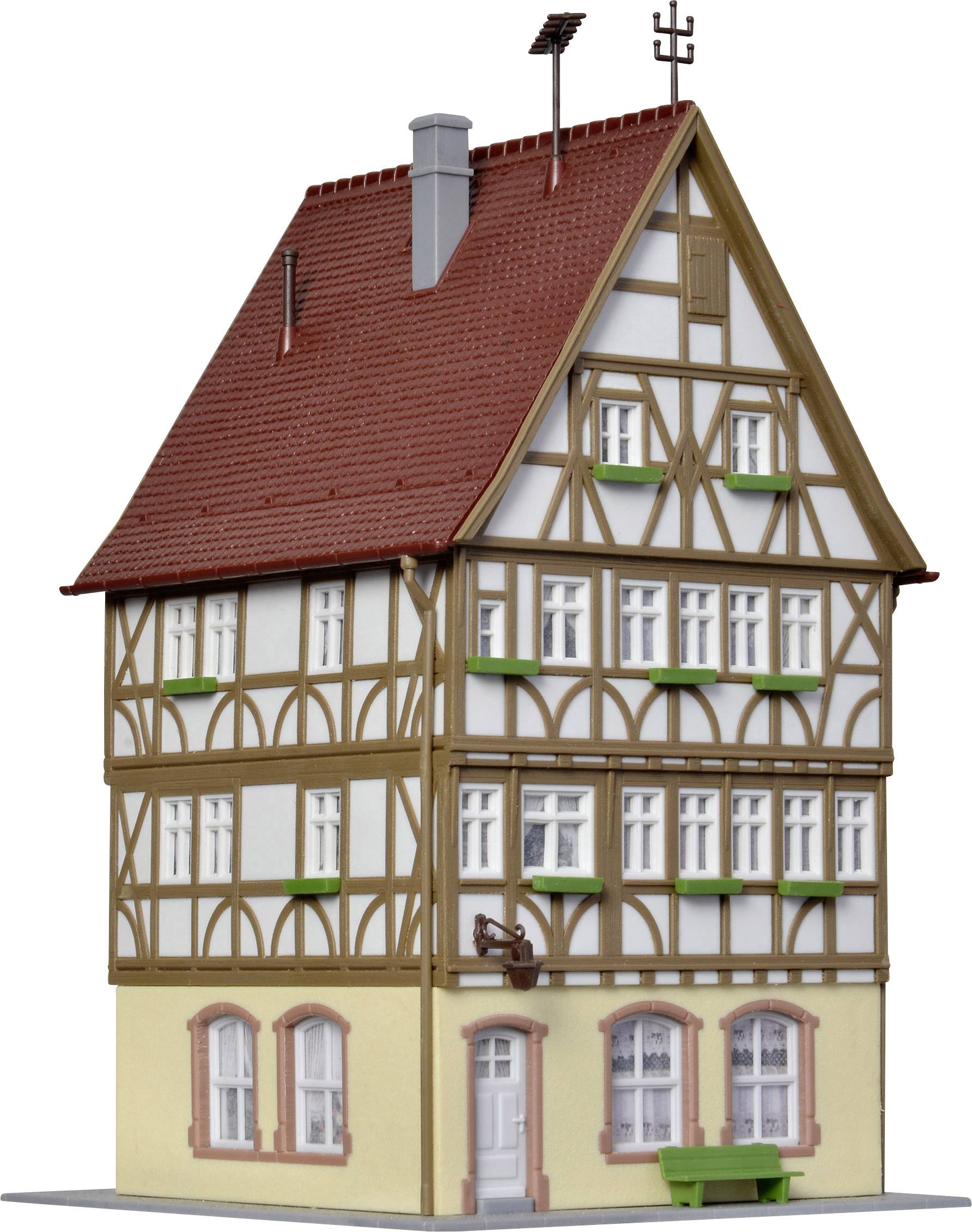 A four-storey half-timbered house with red roof tiles, white windows, and a small green bench in front.