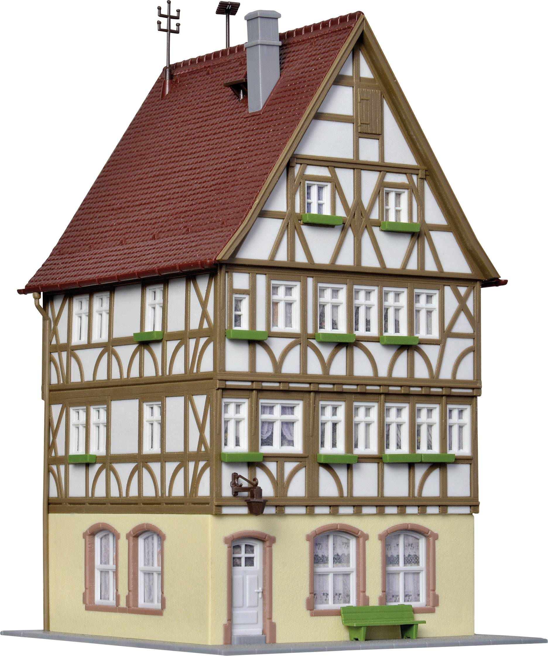 A three-storey half-timbered house with red roof tiles. Green shutters adorn the windows, and a wooden decoration accentuates the architecture.