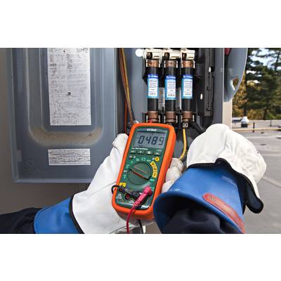 A person is measuring the voltage on fuses with a multimeter. The screen displays 0.489 volts. The person is wearing protective gloves.