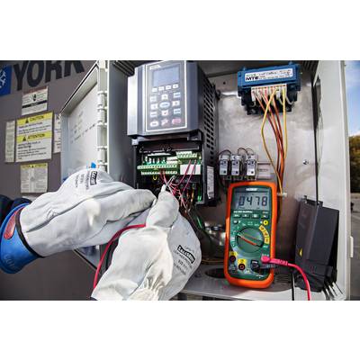 A technician is checking cable connections in an open electrical control cabinet using a digital measuring instrument.