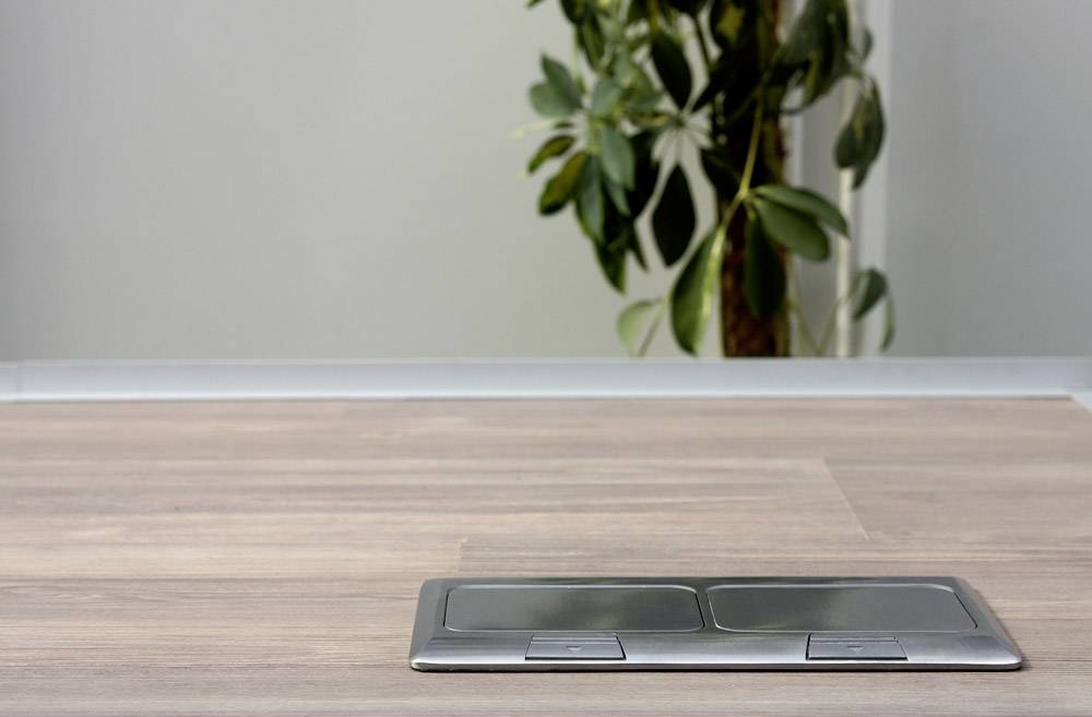 A closed metal floor socket adapter in front of a blurred background with green leaves.