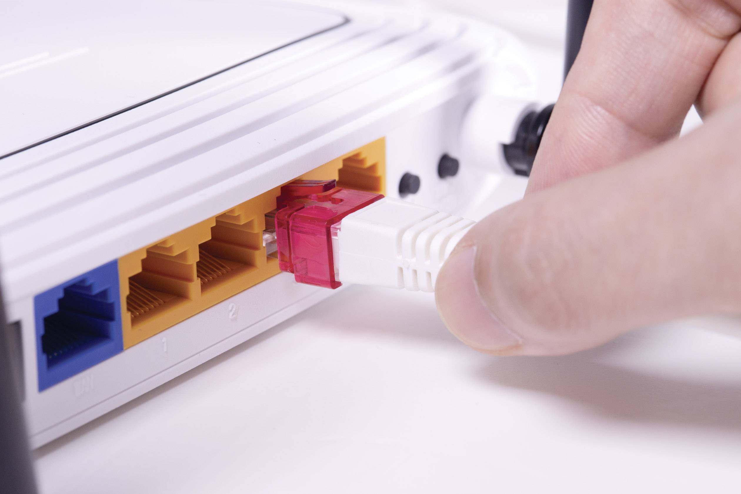A hand is inserting a network cable into a router. The router has multiple LAN ports and is intended for internet connectivity.