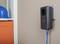 A powerline adapter is plugged into a socket on a wall. A blue Ethernet cable is connected to the adapter. In the background, a blue hard hat and an orange cabinet are visible.