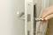 A hand opens a white interior door with a silver door handle. A key is inserted in the lock.