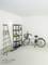 A storage room with a bicycle, ladder, and shelving unit with cleaning supplies. A wall-mounted light illuminates the space.