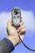 A hand holds an anemometer in the air. The device displays a wind speed of 6.5 metres per second and a temperature of 23.1 degrees Celsius. Blue sky in the background.