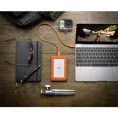 External hard drive connected to laptop on wooden table. Next to laptop are notebook, glasses, pen, camera, and small tripod.