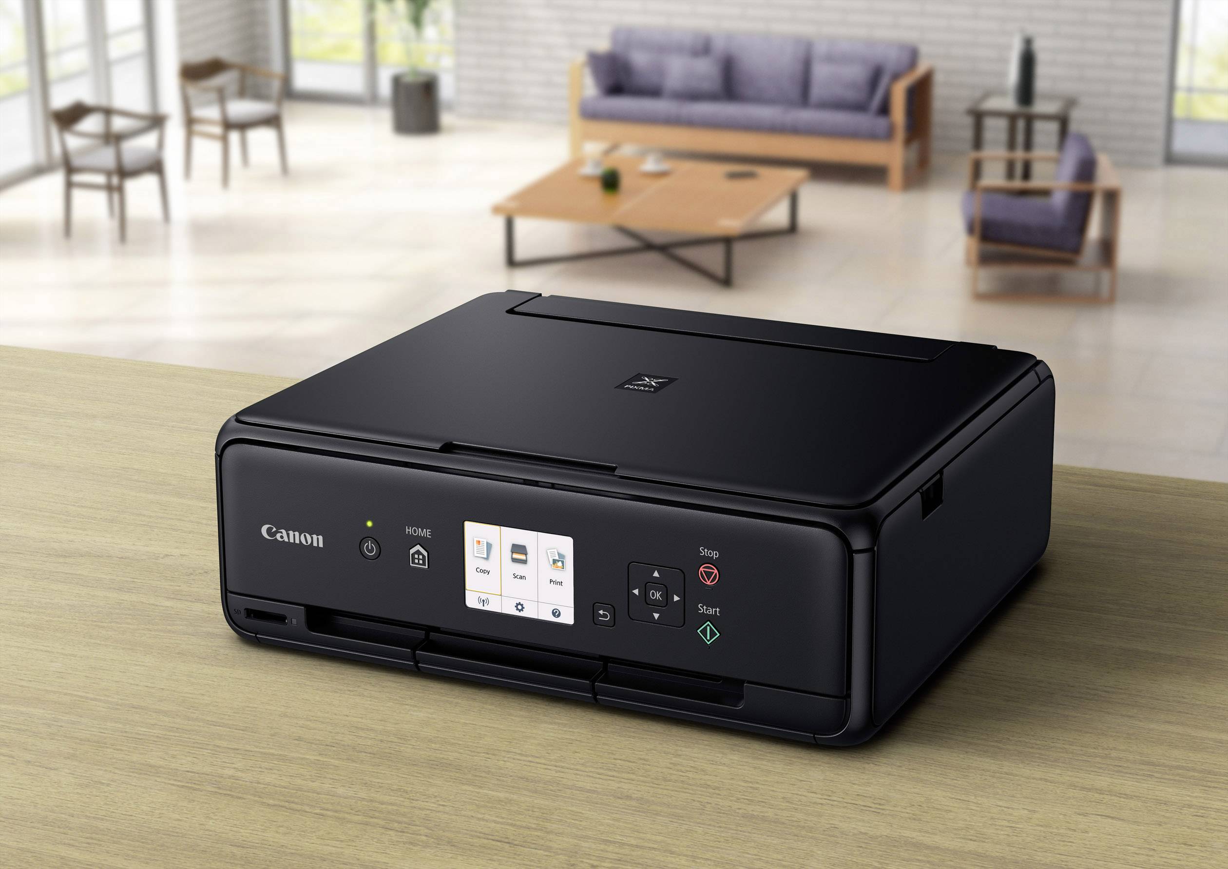 A black printer sits on a table in a modern living room. A sofa and coffee table are visible in the background.