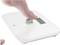 A bare foot is operating a digital scale with a white casing and a display showing weight in kilograms.