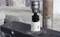 A drill with a hole saw attachment drills into a metal plate, with metal shavings around the hole. Workshop settings are blurred in the background.