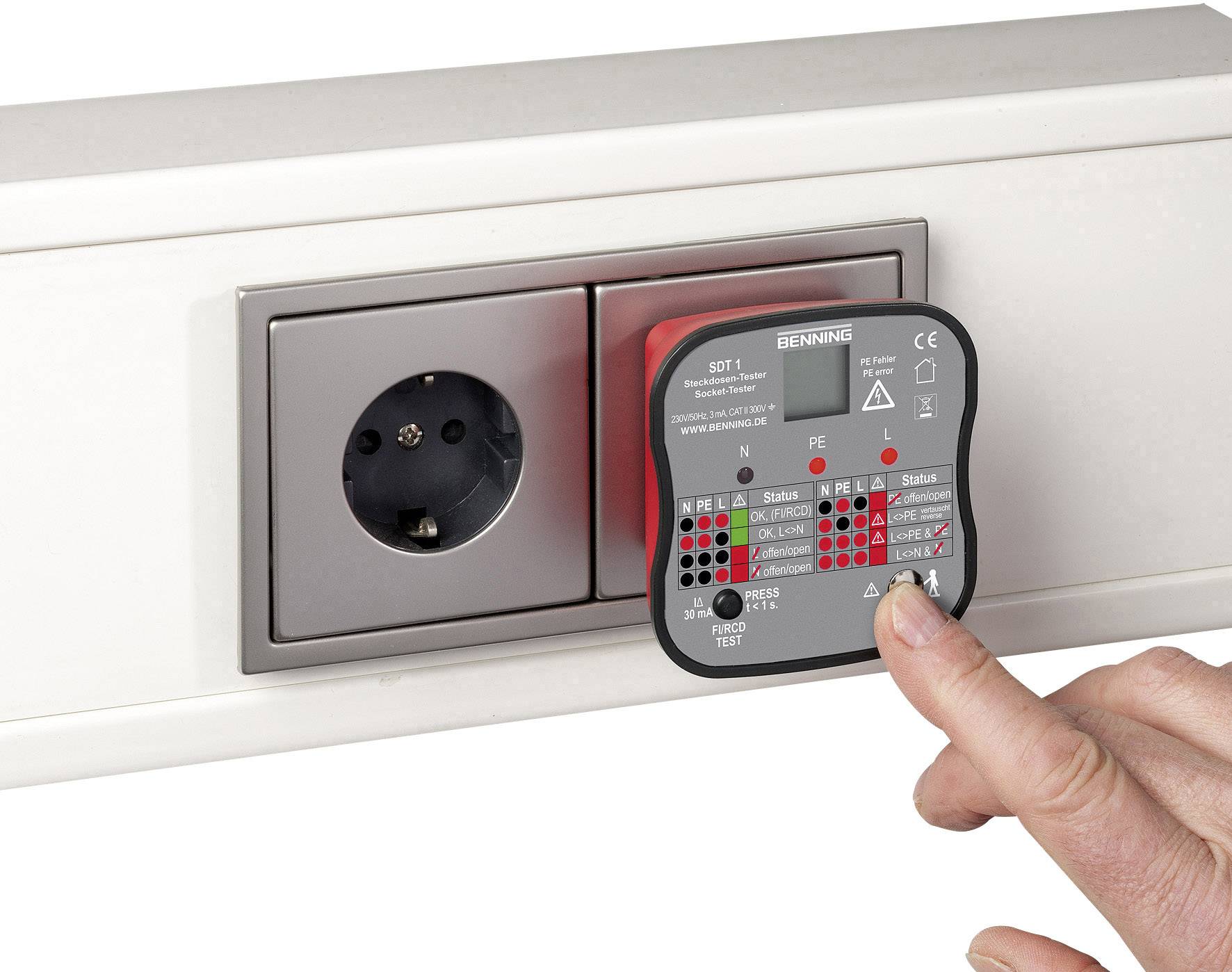 A hand holds a testing device against a power socket. The device displays test results with coloured LED indicators.