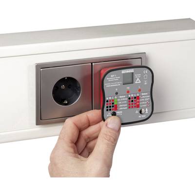 A hand holds a testing device against a wall socket. The device displays electrical safety results through coloured LEDs.