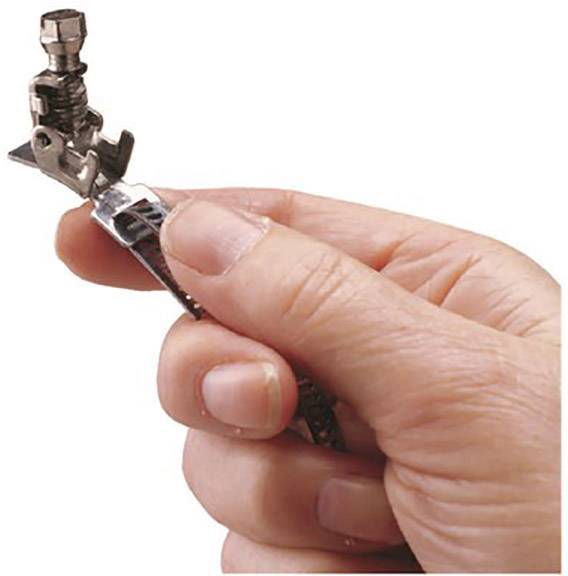 A hand is holding a metal object that looks like a machine part, possibly the foot of a sewing machine.