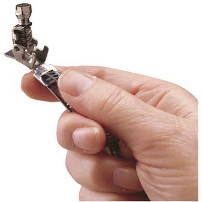 A hand is holding a metal object that looks like a machine part, possibly the foot of a sewing machine.
