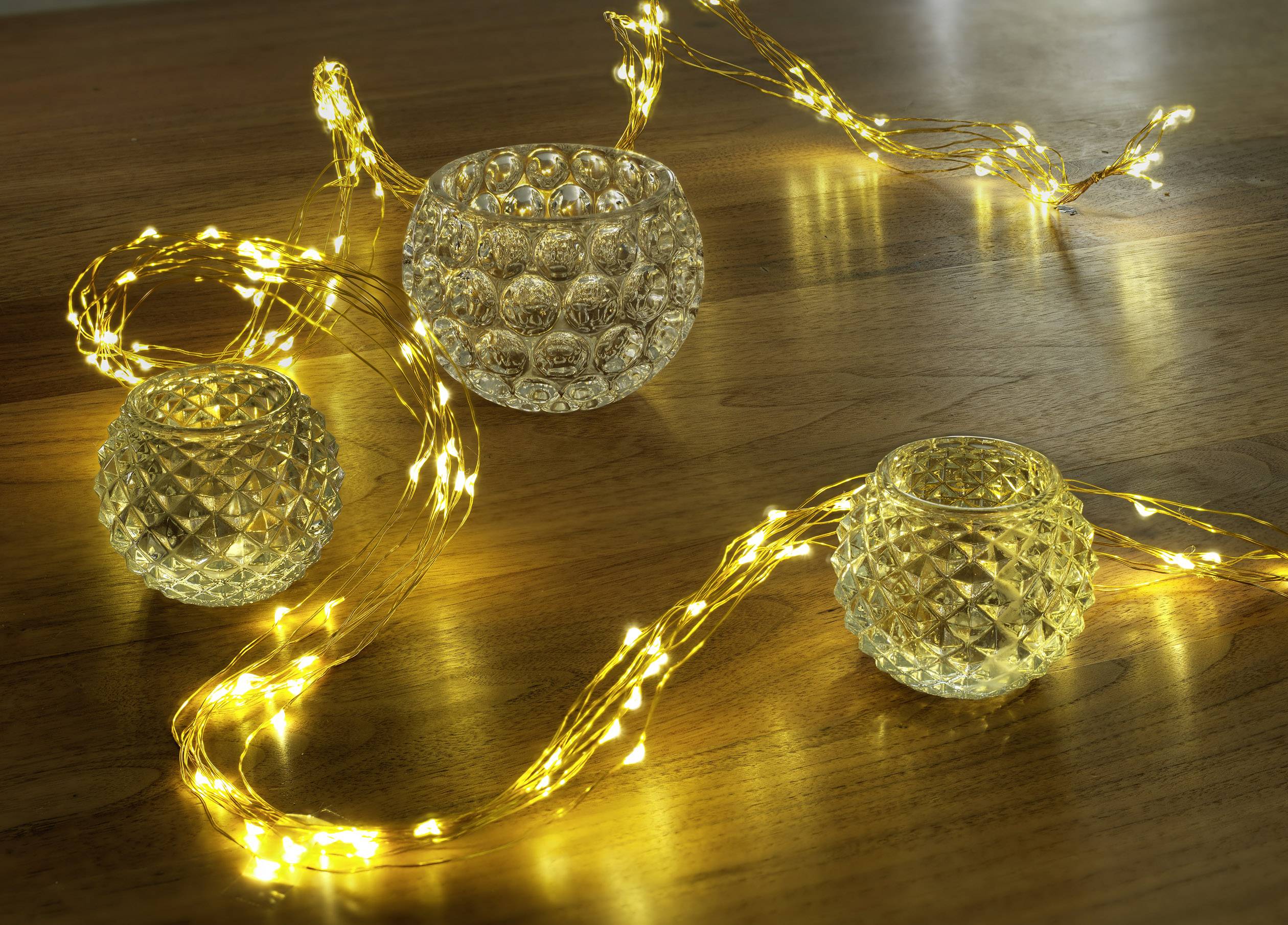 Glass lanterns and yellow fairy lights on a wooden table create a warm, atmospheric lighting.