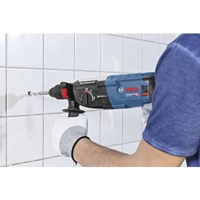 A person is drilling a hole in a white tiled wall using a blue Bosch drill, wearing white gloves.