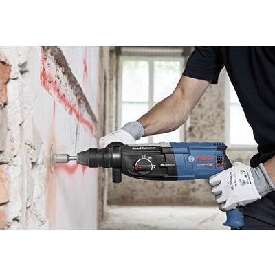 A person is using a BOSCH drill hammer to bore into a concrete wall covered in red dust. Gloves are protecting their hands.