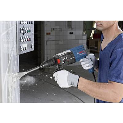 'A person wearing a blue shirt and grey gloves is working with a drill hammer on a wall in an industrial space.'