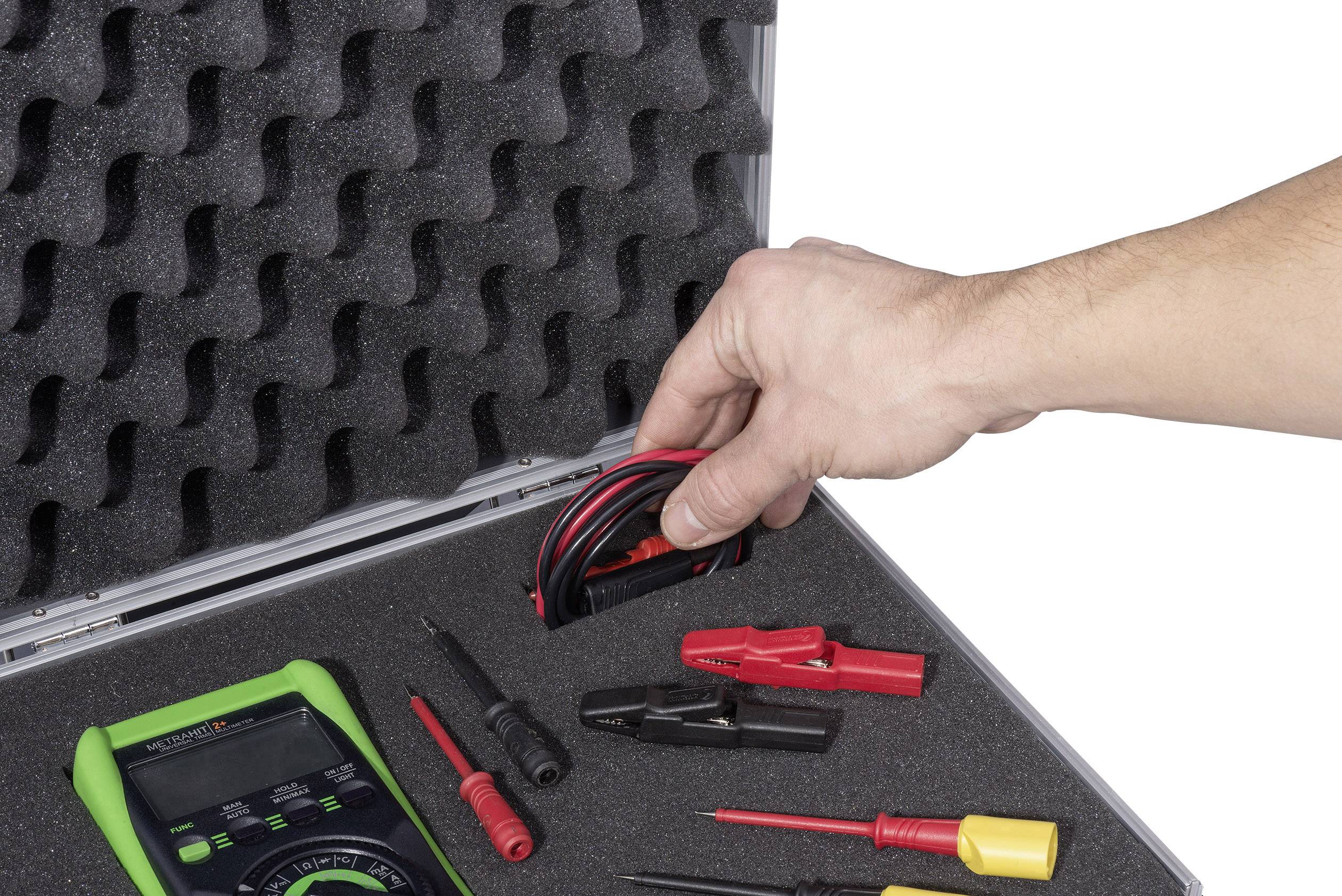 A case with foam lining contains a multimeter and various electrical testing tools. A hand is lifting a cable.