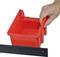 A hand is stacking a red plastic container on a black shelf.