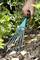 A person is raking earth with a blue hand rake in a garden. Some leaves are lying on the ground.