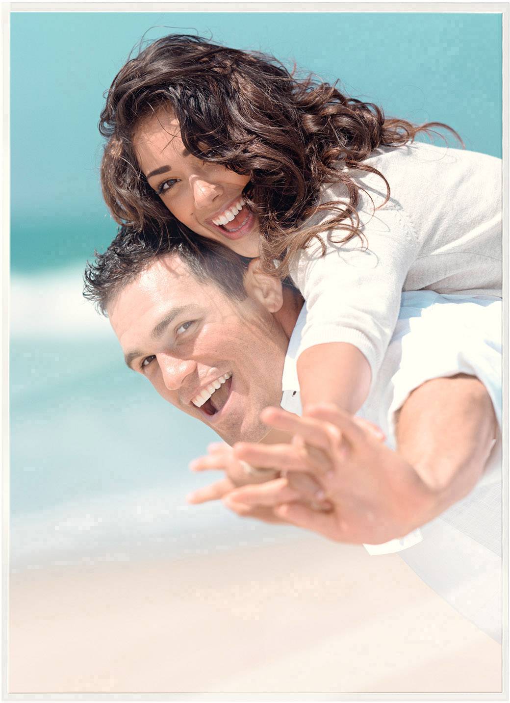 A cheerful couple on the beach; the woman is laughing and has her arms around the man as they both look at the camera.