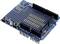 Arduino Shield with a blue circuit board, multiple connection slots and two buttons. Designed for expanding Arduino projects.