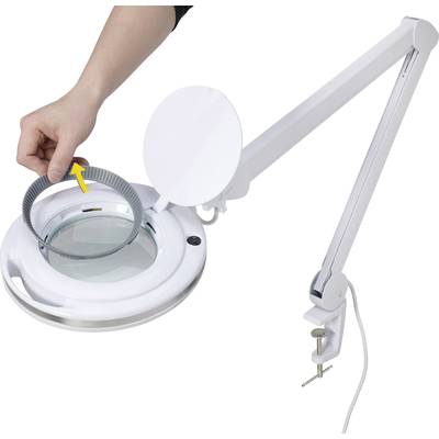 A hand is securing a circular component to a magnifying lamp with an adjustable arm, which is mounted on a table.