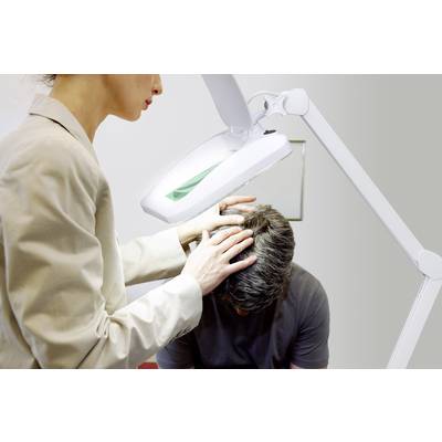 A person is examining the scalp of a seated man using an illuminated magnifying glass, possibly during a medical examination.