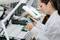 An engineer in a white lab coat inspects a circuit board under a magnifying lamp in a laboratory.