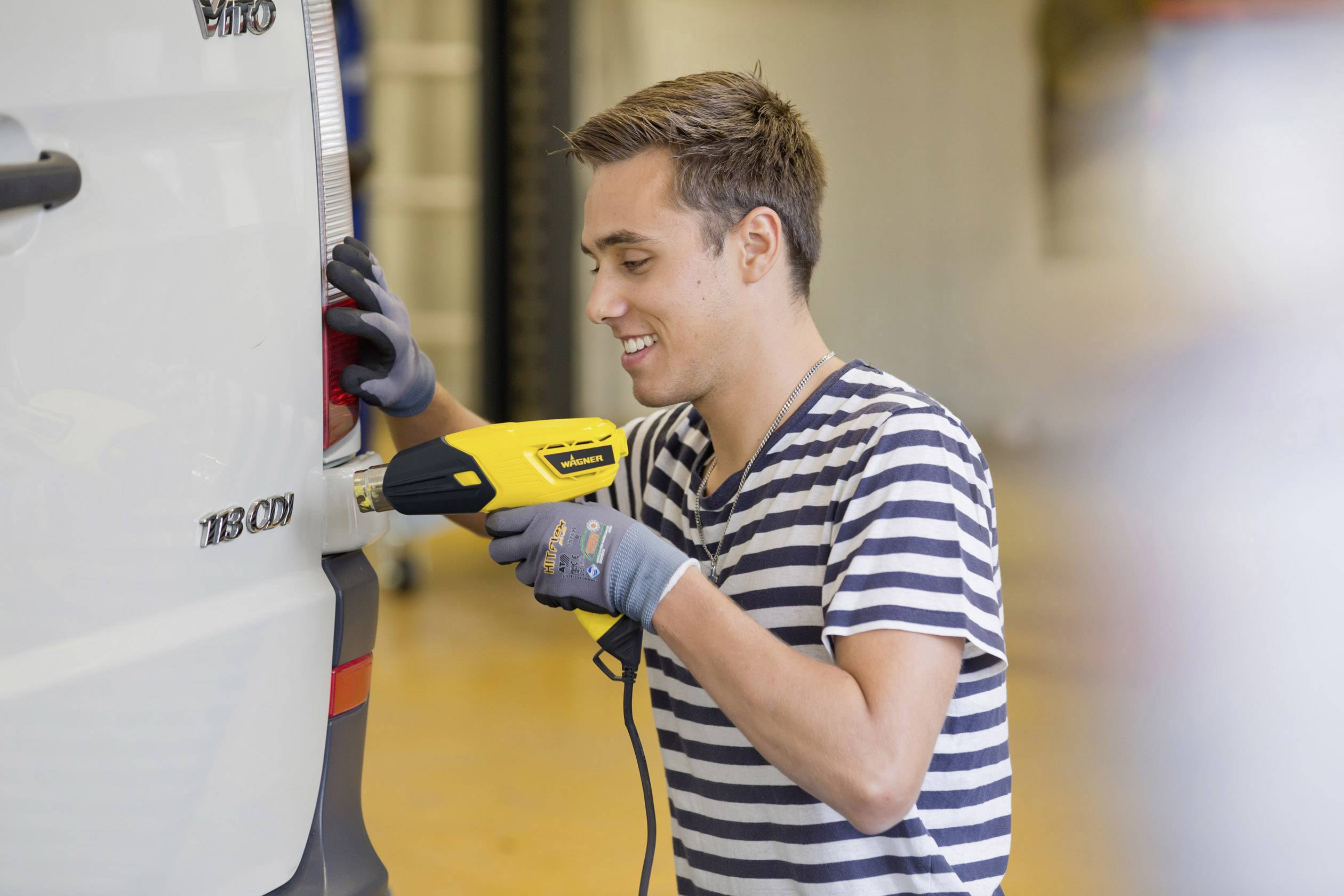 A man is removing the lettering from a white car using a hot air dryer.