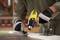 A person is removing old paint from a wooden surface using a yellow hot air gun and a brush, wearing work gloves.