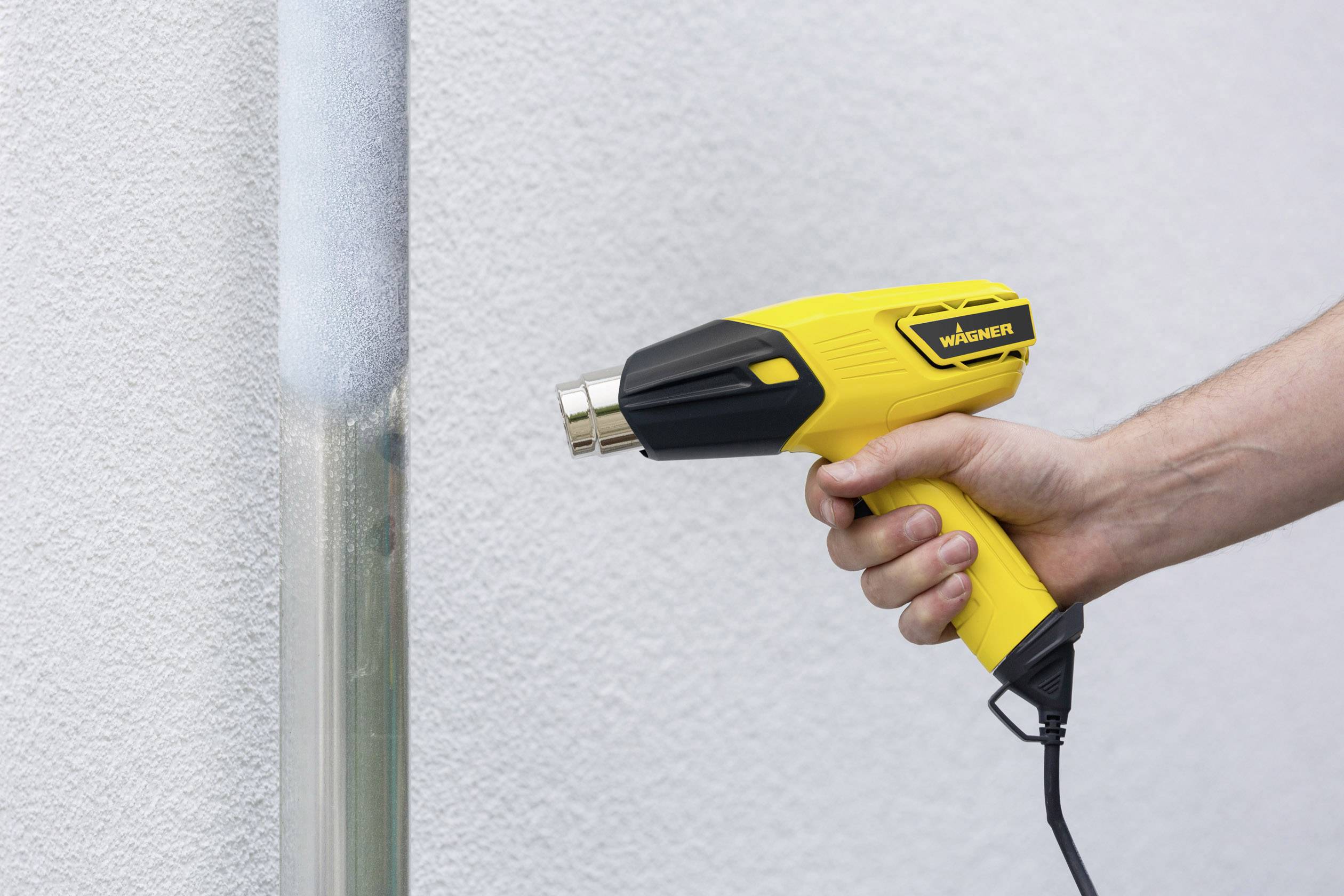 A person is holding a yellow hot air blower against a vertical pipe to heat and shape the coating.
