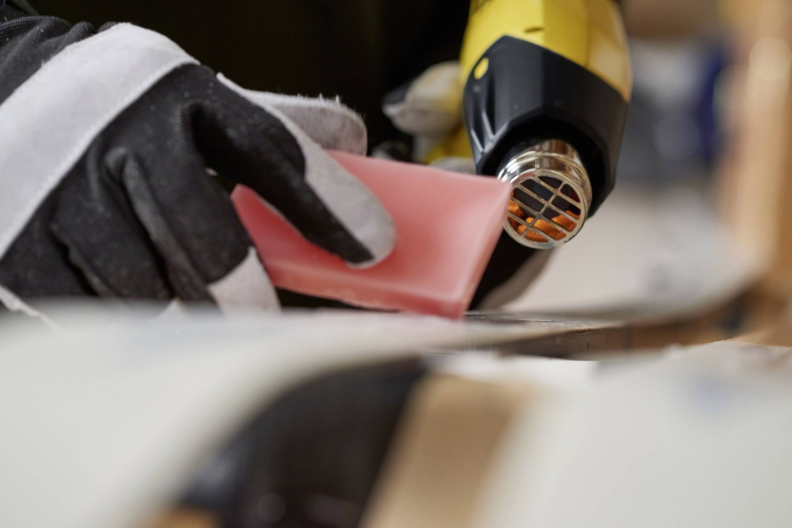A person heats wax with a heat gun on a ski. Gloves protect the hands during the work.