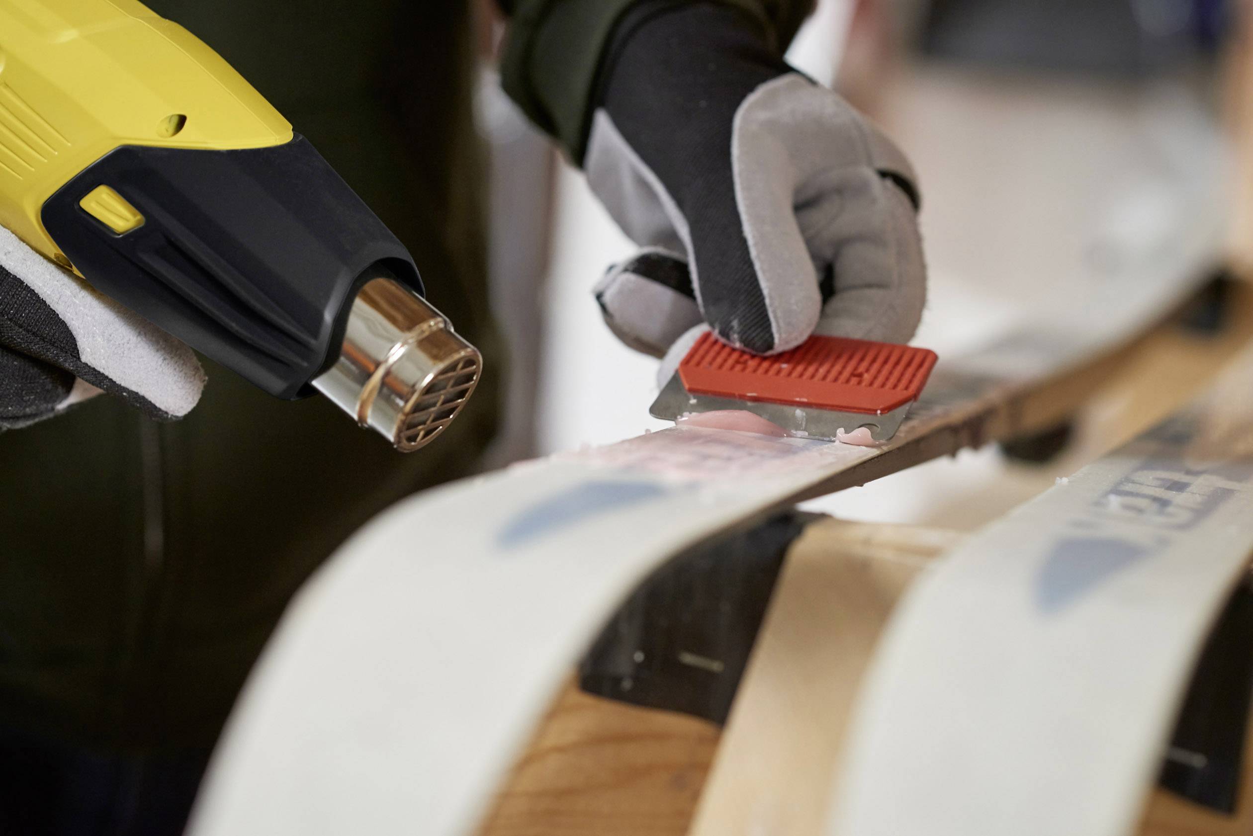 A person is waxing skis with a heating device and scraper, preparing them for use.