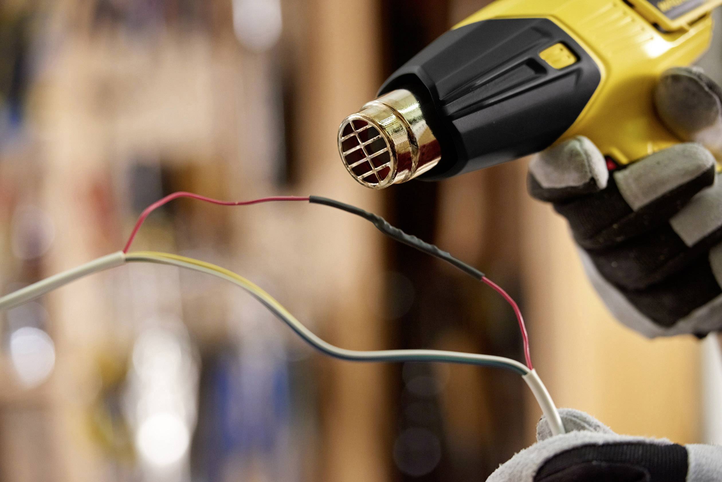 A person is holding a yellow heat gun aimed at a heat-shrink tube to connect cables together.