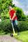 A man wearing safety glasses uses an electric garden tool to trim lawn edges on a well-maintained lawn.