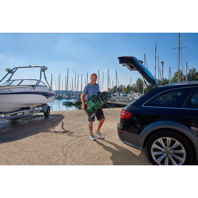 A man is loading golf clubs into the boot of a car, with a marina full of boats in the background on a sunny day.